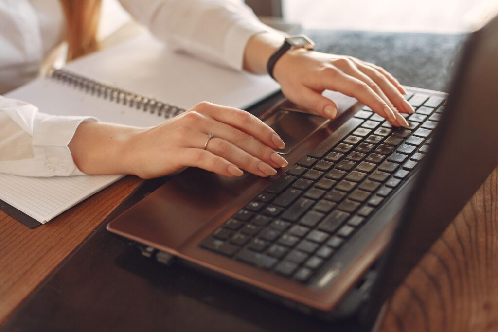 Close-up of a person typing on a laptop with a notebook nearby, ideal for remote work concepts.